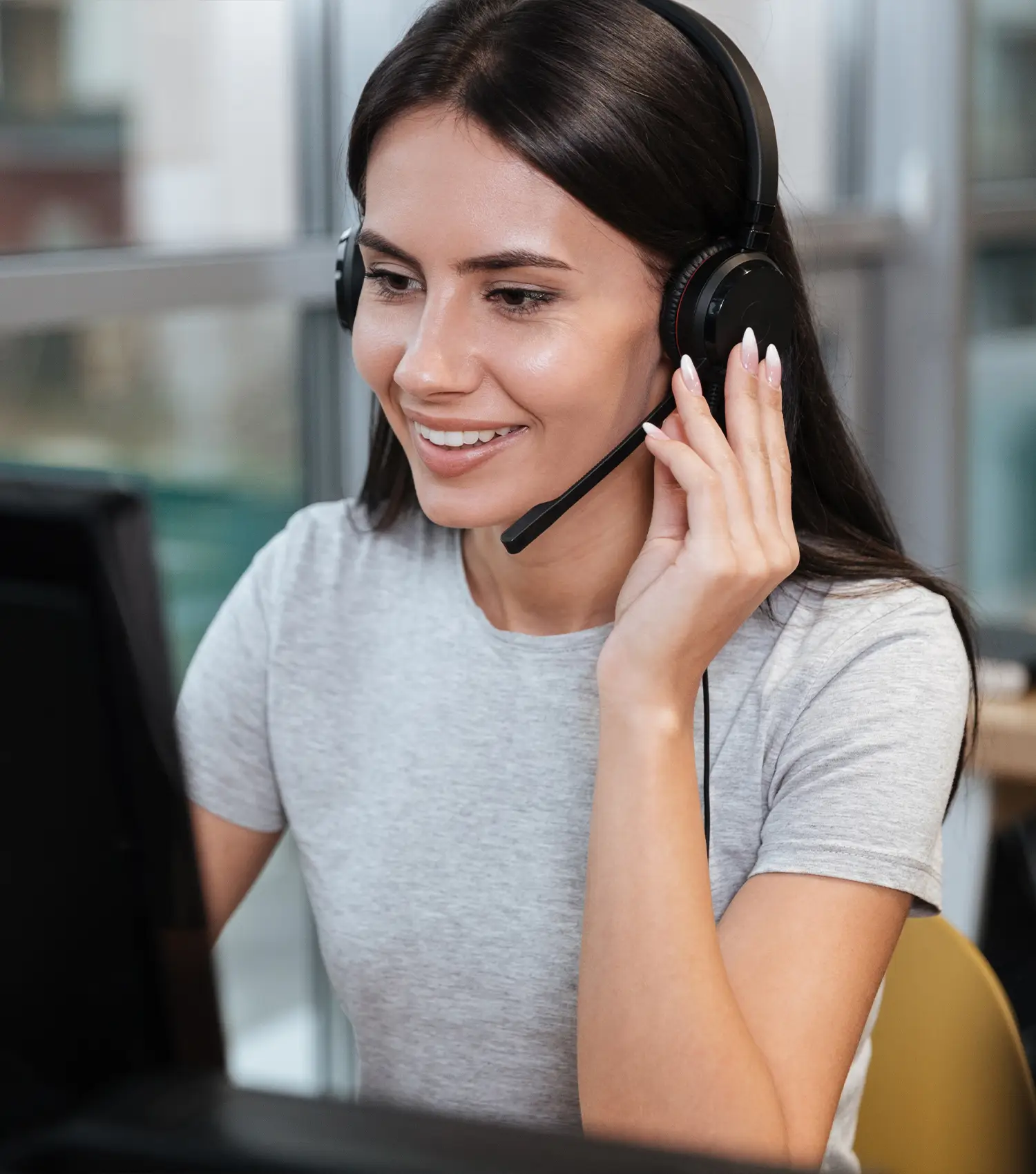 A woman with black hair in a call centre, smiling as she speaks with the customer on the phone.